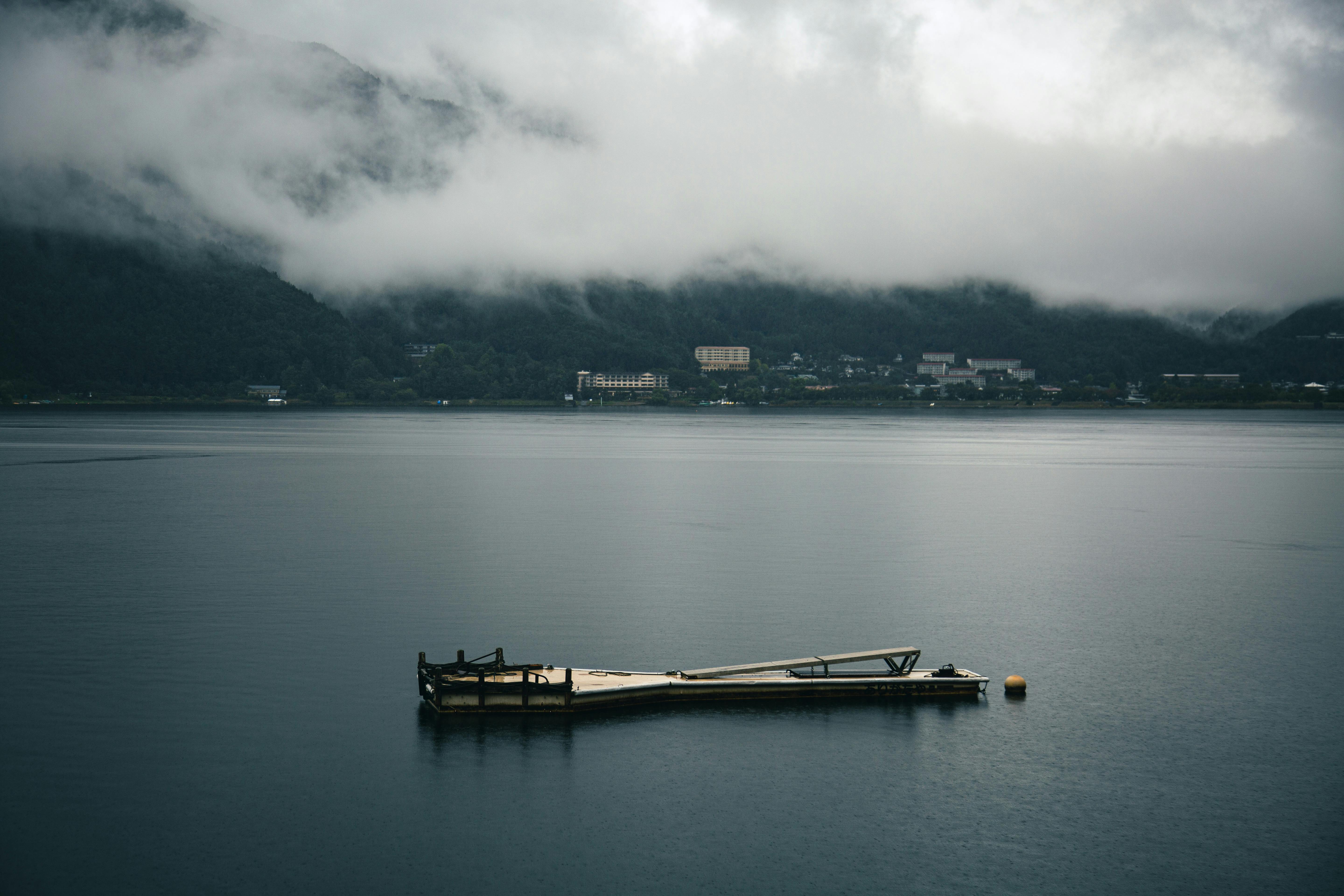 Tranquil view of Kawaguchiko Lake surrounded by misty mountains and a floating dock. Calm and peaceful setting.